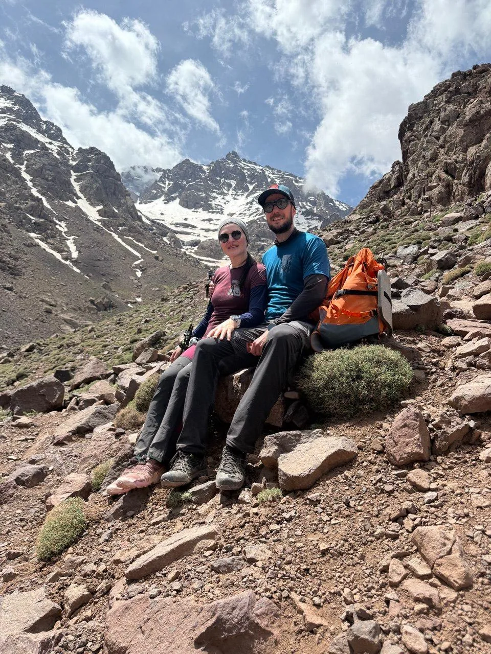 Two travellers resting on the trail beneath the snow-capped peak of Mount Toubkal