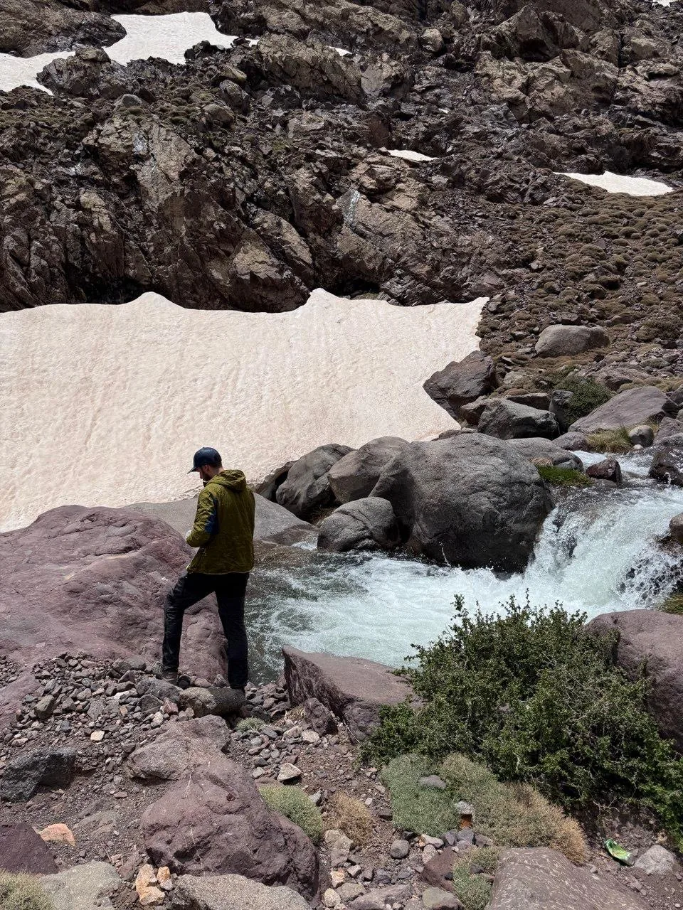Trekker crossing a rushing snowmelt stream in the High Atlas