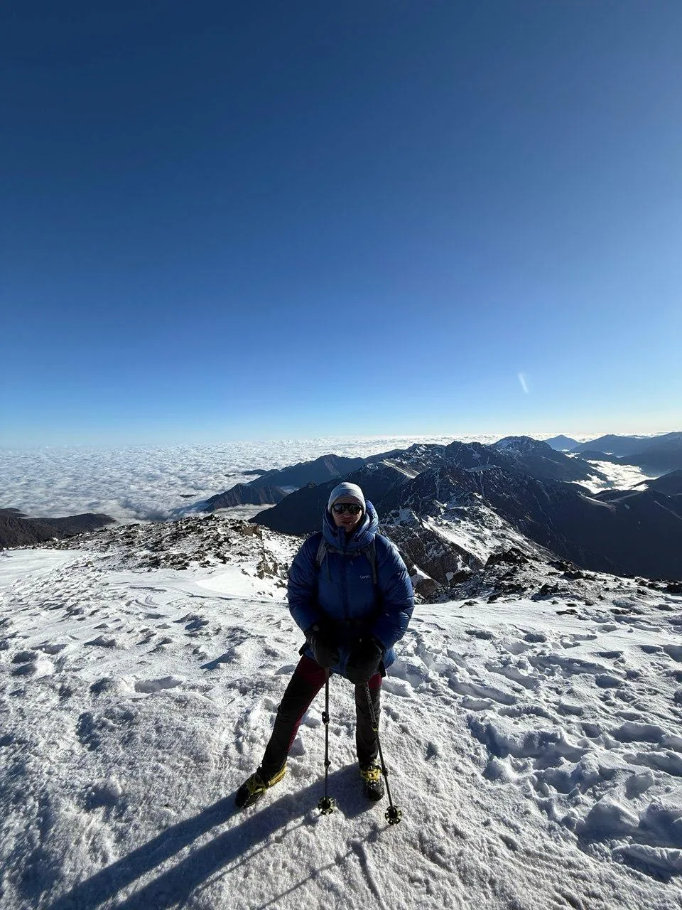 Solo trekker on the snow-covered Toubkal summit ridge above a sea of cloud